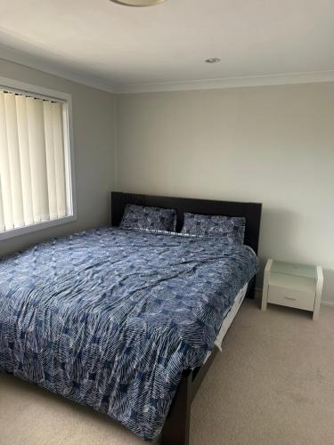 ein Schlafzimmer mit einem Bett mit blauer Decke und einem Fenster in der Unterkunft Luxurious and spacious home in taree in Taree