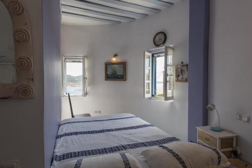 a white bedroom with a bed and two windows at Villa Marie-Iphigenie in Antiparos