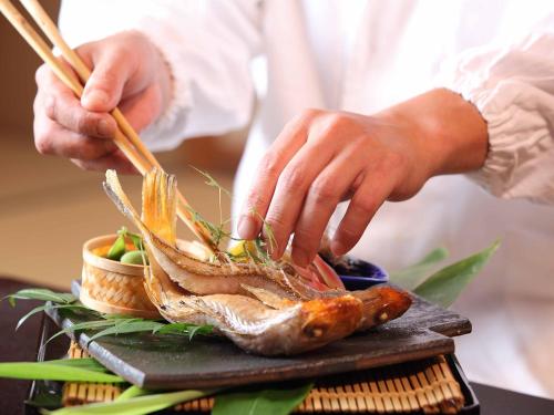 a person preparing a fish on a plate with chopsticks at Choseikan in Agano
