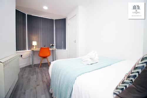 a white bedroom with a bed and a orange chair at Modern 2 Bed Apartment - Near City Centre - By EKLIVING LUXE in Cardiff