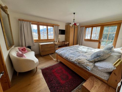 a bedroom with a bed and a chair and windows at Chalet Alten in Klosters Dorf