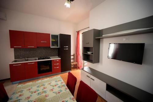 una cucina con armadi rossi, tavolo e televisore di Vivi Salento - Scala di Furno Porto Cesareo a Porto Cesareo