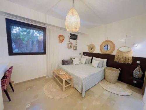 Schlafzimmer mit einem Bett, einem Tisch und einem Fenster in der Unterkunft Appartement cosy et calme avec jardin et piscine in Marrakesch
