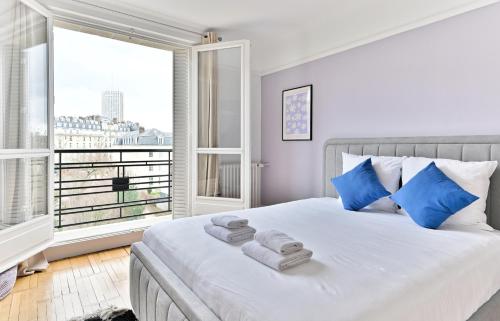 een slaapkamer met een bed met blauwe kussens en een raam bij Appartement luxueux Porte Maillot - Neuilly -II in Neuilly-sur-Seine