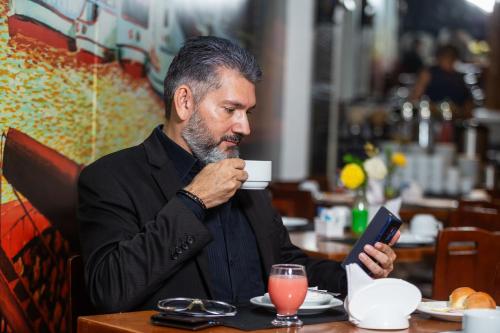 a man sitting at a table drinking a cup of coffee and using a tablet at ibis Styles Belém do Pará in Belém