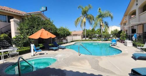 a pool with an umbrella and chairs and a building at Garden Inn and Suites Fresno in Fresno