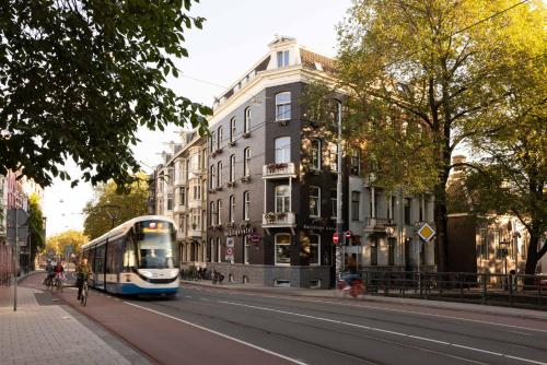 a bus driving down a city street with a building at Backstage Hotel Amsterdam in Amsterdam