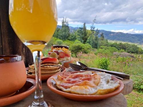 una mesa con platos de comida y un vaso de zumo de naranja en Chigüa Glamping, en Ráquira