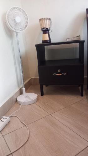 a black dresser with a fan and a lamp at Mini Lookout Entebbe in Entebbe