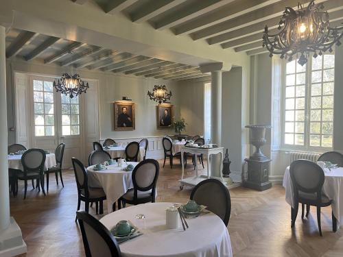 uma sala de jantar com mesas e cadeiras brancas e janelas em Hôtel du Château du Bois-Guibert em Bonneval