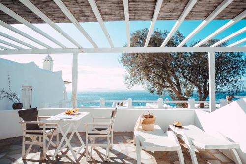 een patio met witte tafels en stoelen en uitzicht op de oceaan bij With-inn Mykonos Suites in Tourlos