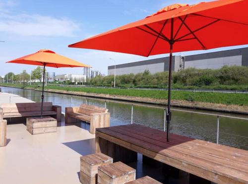 two benches with red umbrellas next to a river at Bed in Boat in Ypres