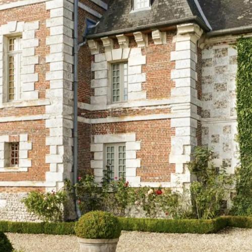 un vieux bâtiment en briques avec des fleurs devant lui dans l'établissement Domaine du Bosc Roger, à Bouquetot