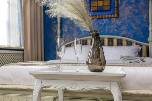 two wine glasses and a vase on a table next to a bed at Kurpiai - Suites & SPA in Klaipėda