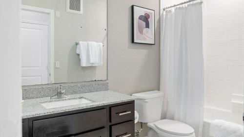 een badkamer met een wastafel, een toilet en een spiegel bij Landing - Modern Apartment with Amazing Amenities (ID1192X099) in Kissimmee