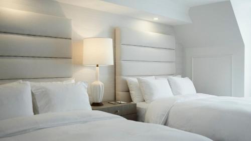 two beds in a bedroom with white sheets and a lamp at Chateau Vaudreuil in Vaudreuil-Dorion