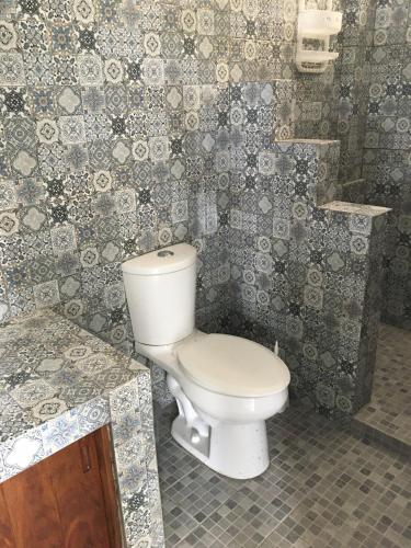 a bathroom with a toilet in a tiled wall at Buda Blanca 5 min caminando a la playa in Cuatunalco