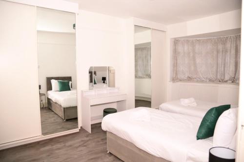Habitación blanca con 2 camas y espejo. en Star London Golders Rise Luxury 4-Bed Oasis with Garden, en Hendon