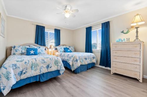 twee bedden in een slaapkamer met blauwe gordijnen bij Beach D-ehs Brunswick Vacation Rentals in Ocean Isle Beach