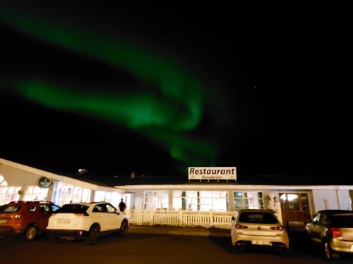 a building with cars parked in a parking lot under the green northern lights at Kanslarinn Hostel in Hella
