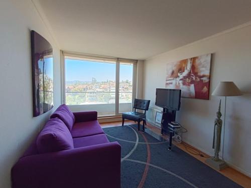 a living room with a purple couch and a large window at APART LOMAS DE SAN ANDRES concepción in Concepción