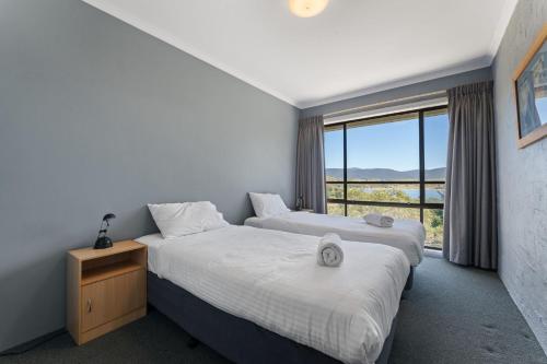 two beds in a room with a large window at Alpine Mountain View 18 - 4BR l Mountain Views l Swimming Pool l Air-Con l WiFi in Jindabyne