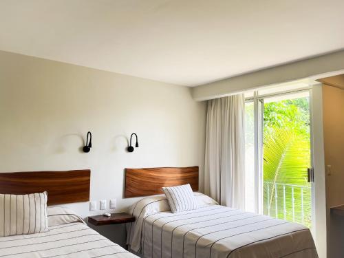 two beds in a hotel room with a window at Hotel Suites Villasol in Puerto Escondido