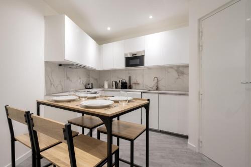 une cuisine avec des armoires blanches et une table et des chaises en bois dans l'établissement Appartement des Colombes - Welkeys, à Courbevoie