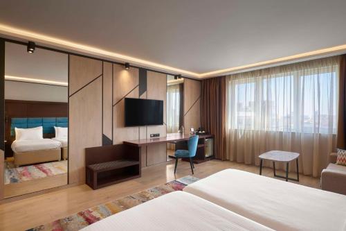 Cette chambre comprend un lit et un bureau avec une télévision. dans l'établissement Hotel Imperial Plovdiv, a member of Radisson Individuals, à Plovdiv