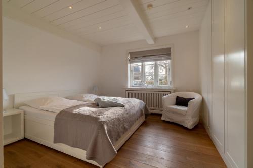 a white bedroom with a bed and a chair at Kapitänshaus Ost in Oldsum