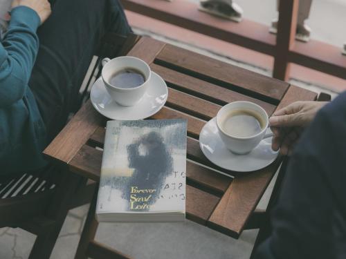 two cups of coffee and a book on a wooden table at Chalet Shiga in Yamanouchi
