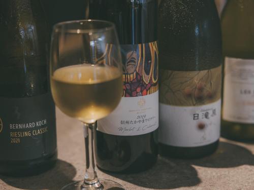 a glass of white wine next to three bottles of wine at Chalet Shiga in Yamanouchi