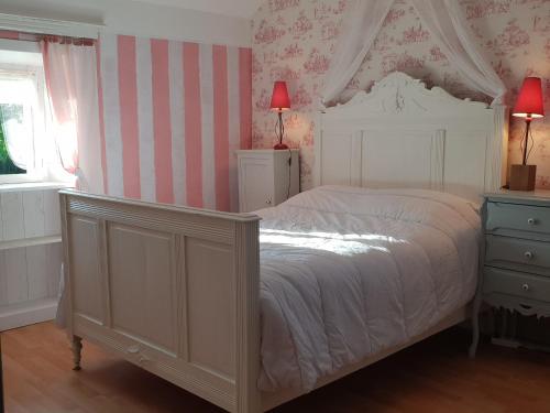 una camera da letto con un letto bianco e carta da parati rosa e bianca di Maison indépendante avec grand jardin, terrasse, plan d'eau sécurisé et salle de jeux près du lac d'Éguzon - FR-1-591-216 a Bazaiges