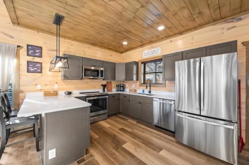 a kitchen with a stainless steel refrigerator and wooden ceilings at SmokiesBoutiqueCabins would love to host you at our NEW cabin! 3 King Suites, Indoor Pool, Game Room, Lounge with 75" TV! Close to Dollywood and the Parkway! in Pigeon Forge