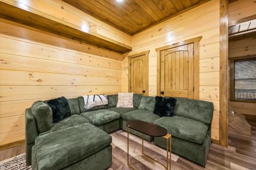 a living room with a green couch and a table at SmokiesBoutiqueCabins would love to host you at our NEW cabin! 3 King Suites, Indoor Pool, Game Room, Lounge with 75" TV! Close to Dollywood and the Parkway! in Pigeon Forge