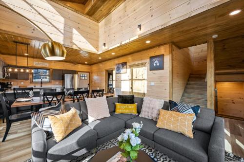 a living room with a gray couch and a table at SmokiesBoutiqueCabins would love to host you at our NEW cabin! 3 King Suites, Indoor Pool, Game Room, Lounge with 75" TV! Close to Dollywood and the Parkway! in Pigeon Forge