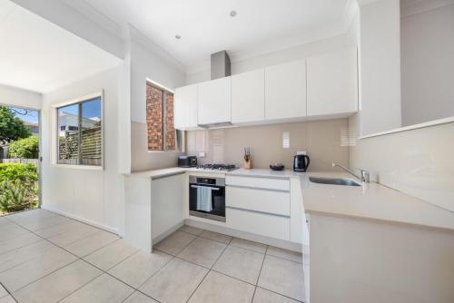 a white kitchen with white cabinets and a window at WINCH9 - Seaside Serenity in Sydney