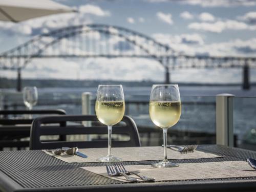 two glasses of white wine on a table with a bridge at Rodd Miramichi in Miramichi