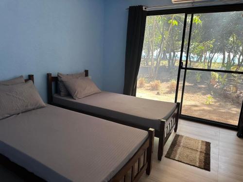 two beds in a room with a large window at Magalong Villa at Holy Land in Busuanga in Busuanga