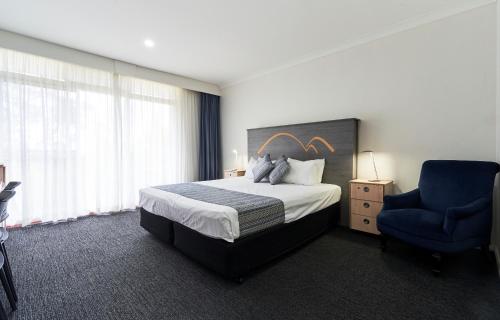 ein Hotelzimmer mit einem Bett und einem blauen Stuhl in der Unterkunft Leura Gardens Resort in Leura