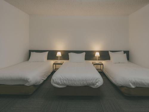 a room with three beds with white sheets and lamps at Chalet Shiga in Yamanouchi