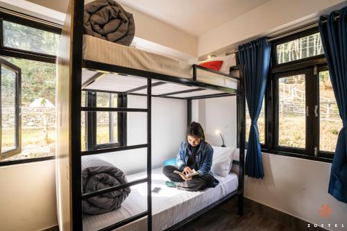 a woman sitting on a bed in a bunk bed room at Zostel Rinchenpong (Pelling) in Rinchingpong