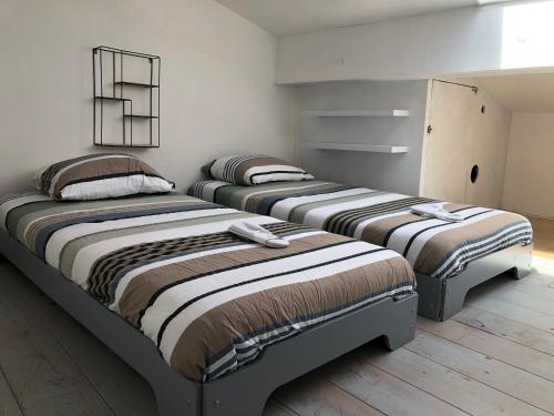 3 łóżka w pokoju z białymi ścianami i drewnianą podłogą w obiekcie Le Petit Relais du Canal w mieście Trèbes