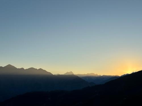 a sunset over a mountain range with the sun setting at Himalayan Canvas khajjiar in Khajjiar 