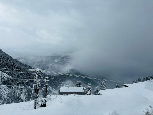 a snow covered mountain with a house in the distance at Himalayan Canvas khajjiar in Khajjiar 