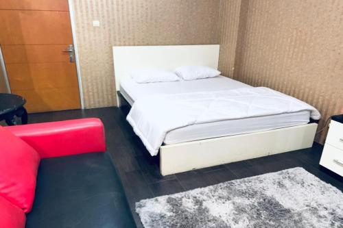 una piccola camera con un letto bianco e un divano rosso di OYO 93585 Apartemen Cibubur Village By Raja Property a Depok
