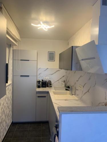 Il comprend une cuisine équipée de comptoirs blancs et d'un réfrigérateur blanc. dans l'établissement Welcome Appart Colmar, à Colmar