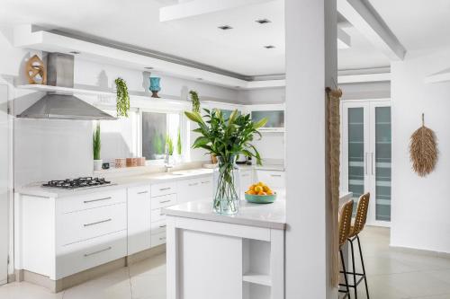 a white kitchen with a vase of flowers on a counter at By Eezy- דירה משפחתית מפנקת 3 חדרי שינה - Hanechoshet in Eilat