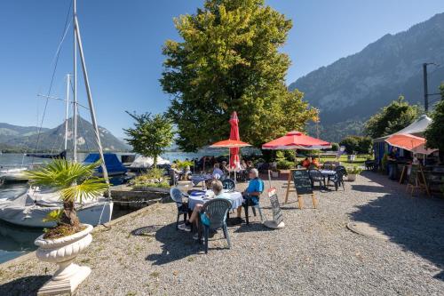 a group of people sitting at tables near a marina at Bijou du Lac - mit Pool und Privatstrand in Därligen