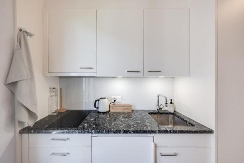 a white kitchen with a sink and white cabinets at Bijou du Lac - mit Pool und Privatstrand in Därligen